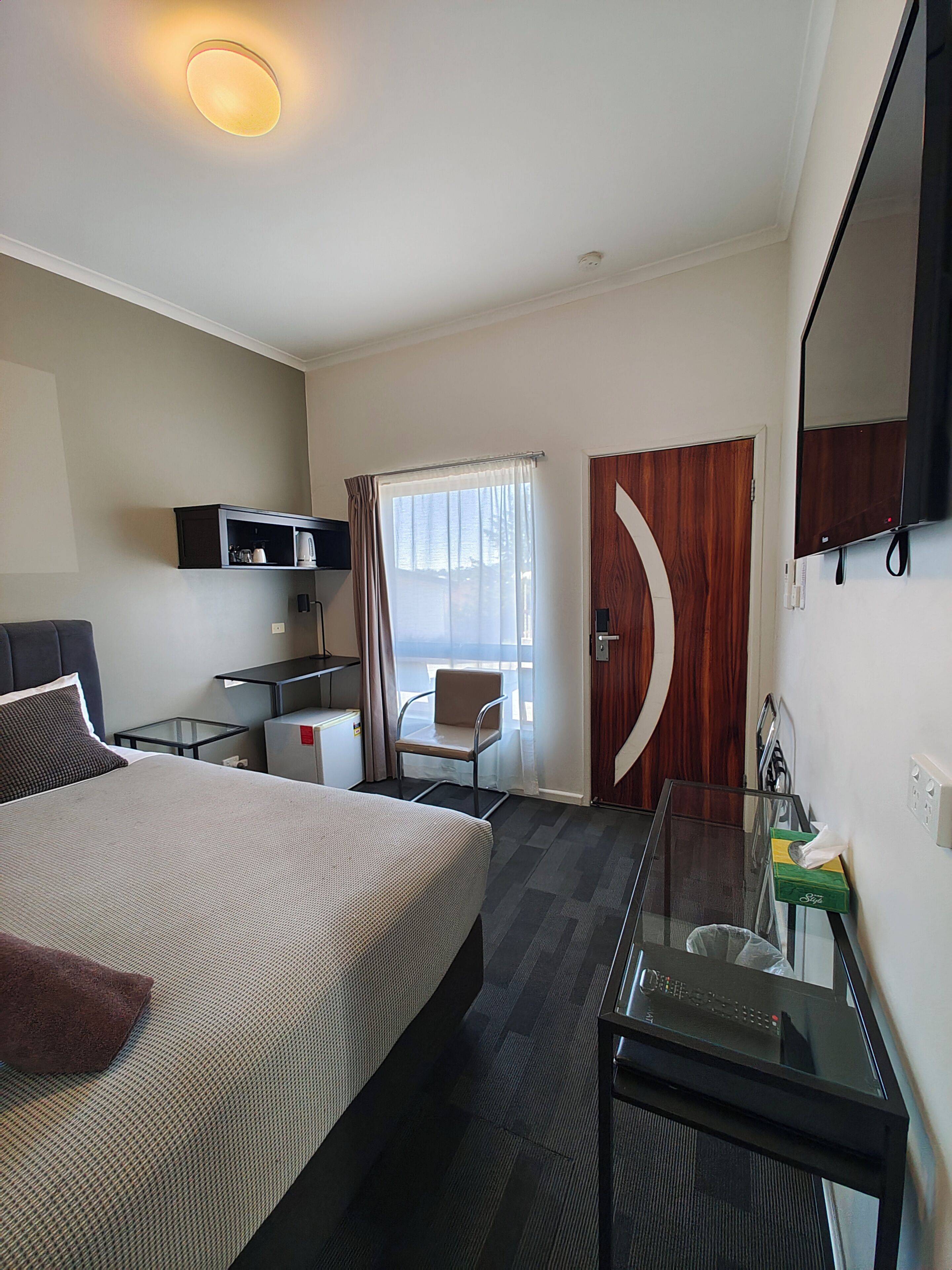 Een hotelkamer met een bed, een bureau met computer, een stoel, een televisie en een raam met gordijnen.
