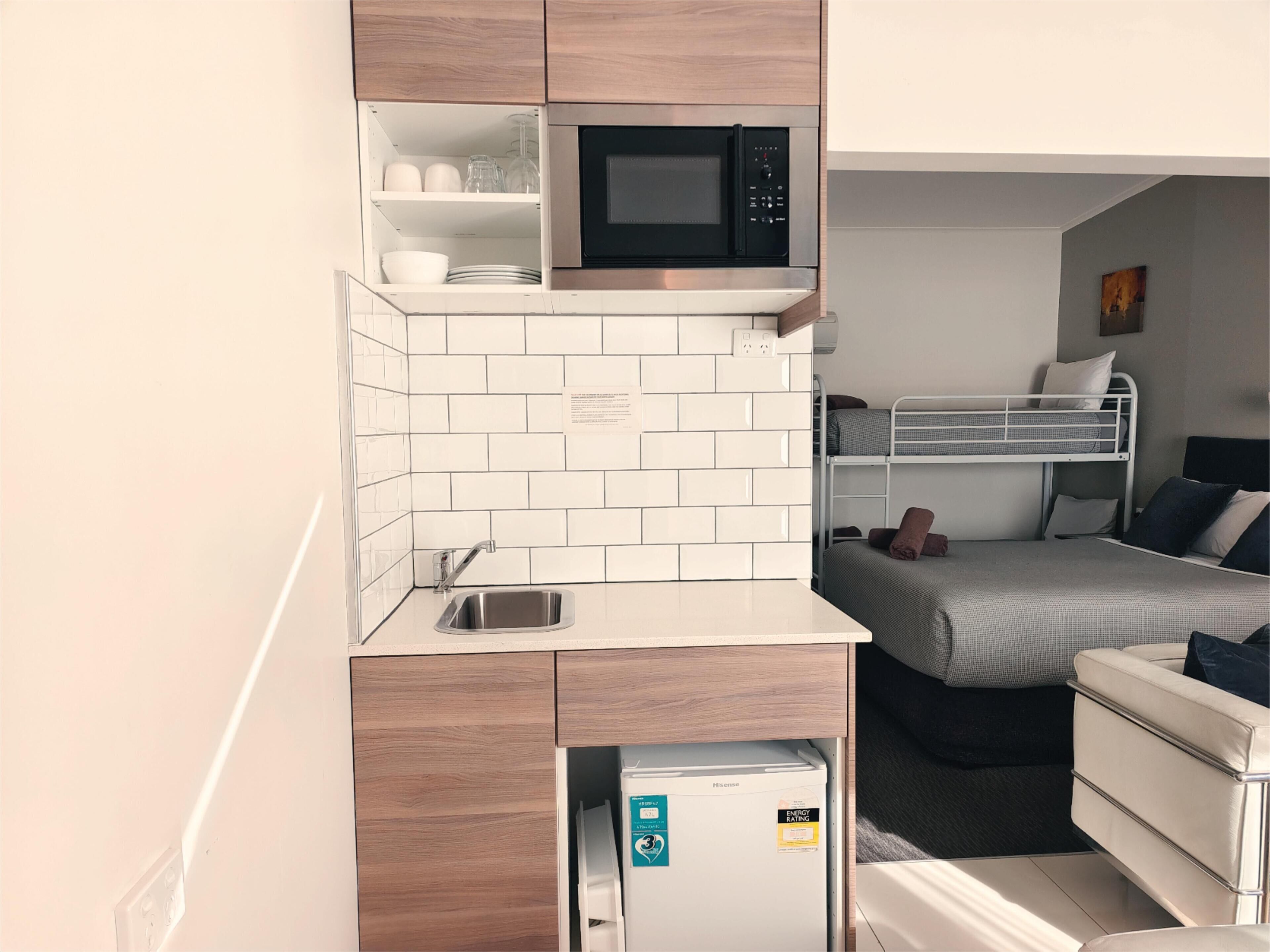 Une petite cuisine équipée d’un four à micro-ondes, d’un évier et d’un réfrigérateur. On y trouve également un lit superposé avec des oreillers et un petit coin salon.