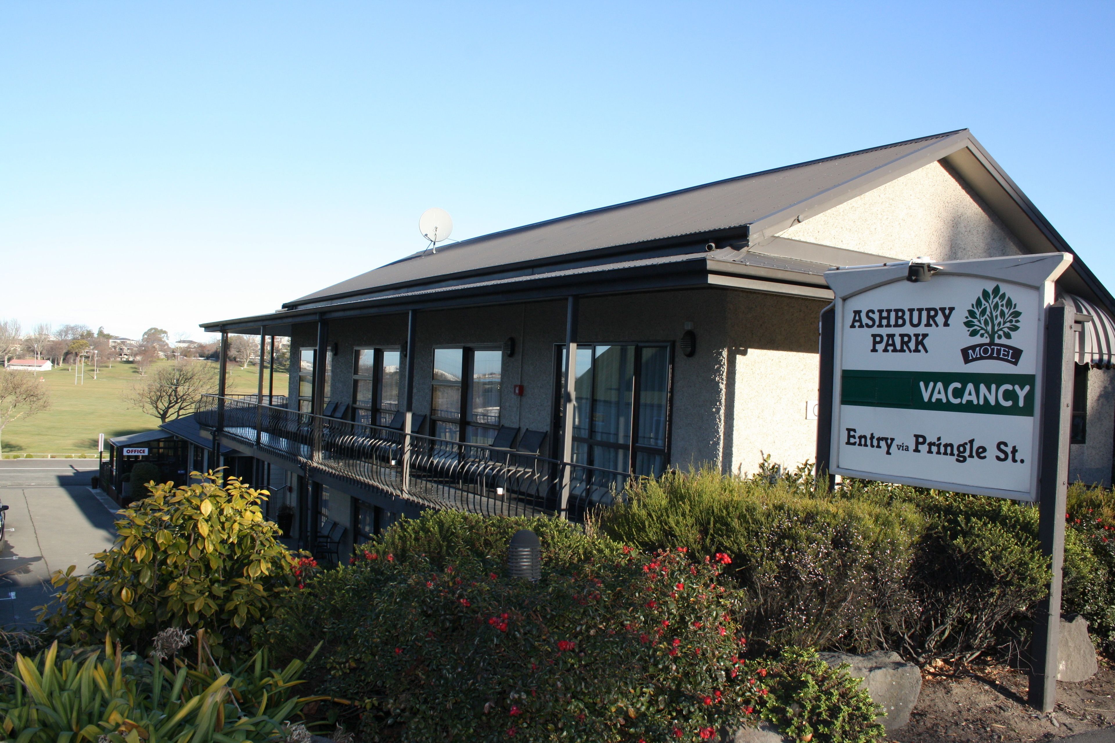 A motel with a covered outdoor seating area, a sign indicating a vacancy, and an entry via Pringle St.