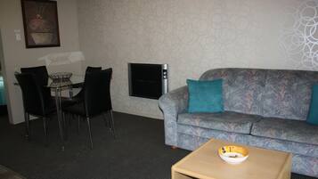 A living room with a sofa, a coffee table, a TV, and a dining area with chairs and a table.