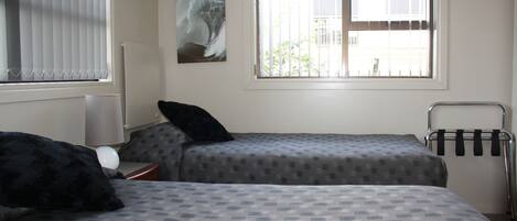A room with two beds, a radiator, a window with blinds, and a towel rack.
