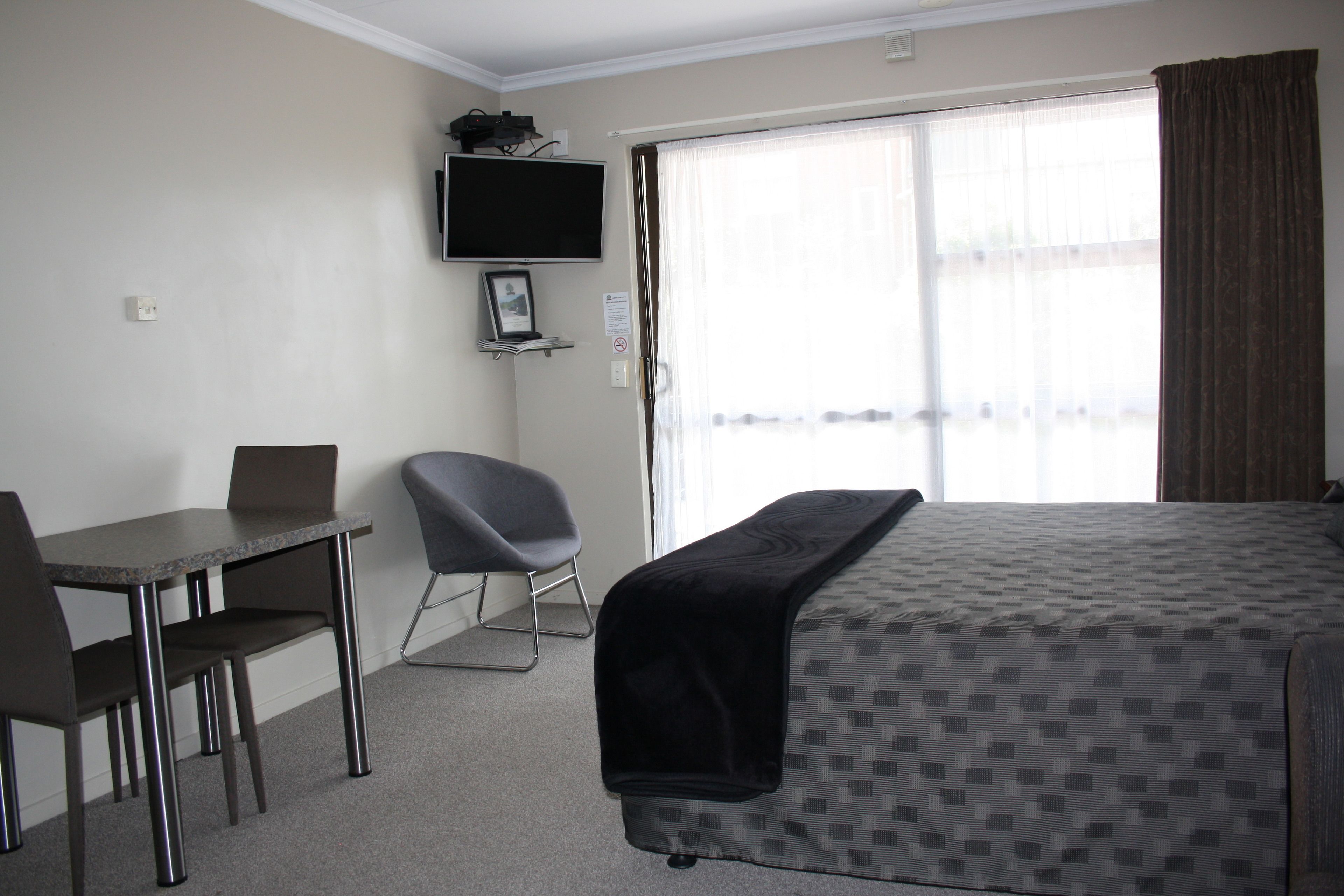 A hotel room with a bed, a desk, two chairs, a television, and a window with curtains.