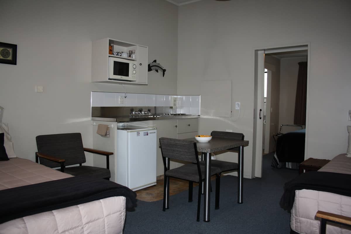 A compact hotel room with a kitchenette, two beds, a dining table, and a small refrigerator.