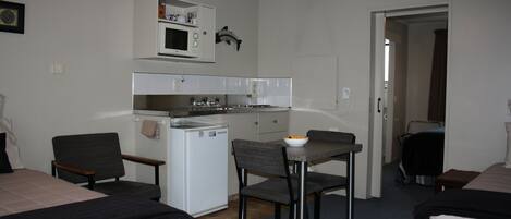 Habitación de hotel compacta con kitchenette, dos camas, una mesa de comedor y un refrigerador pequeño.