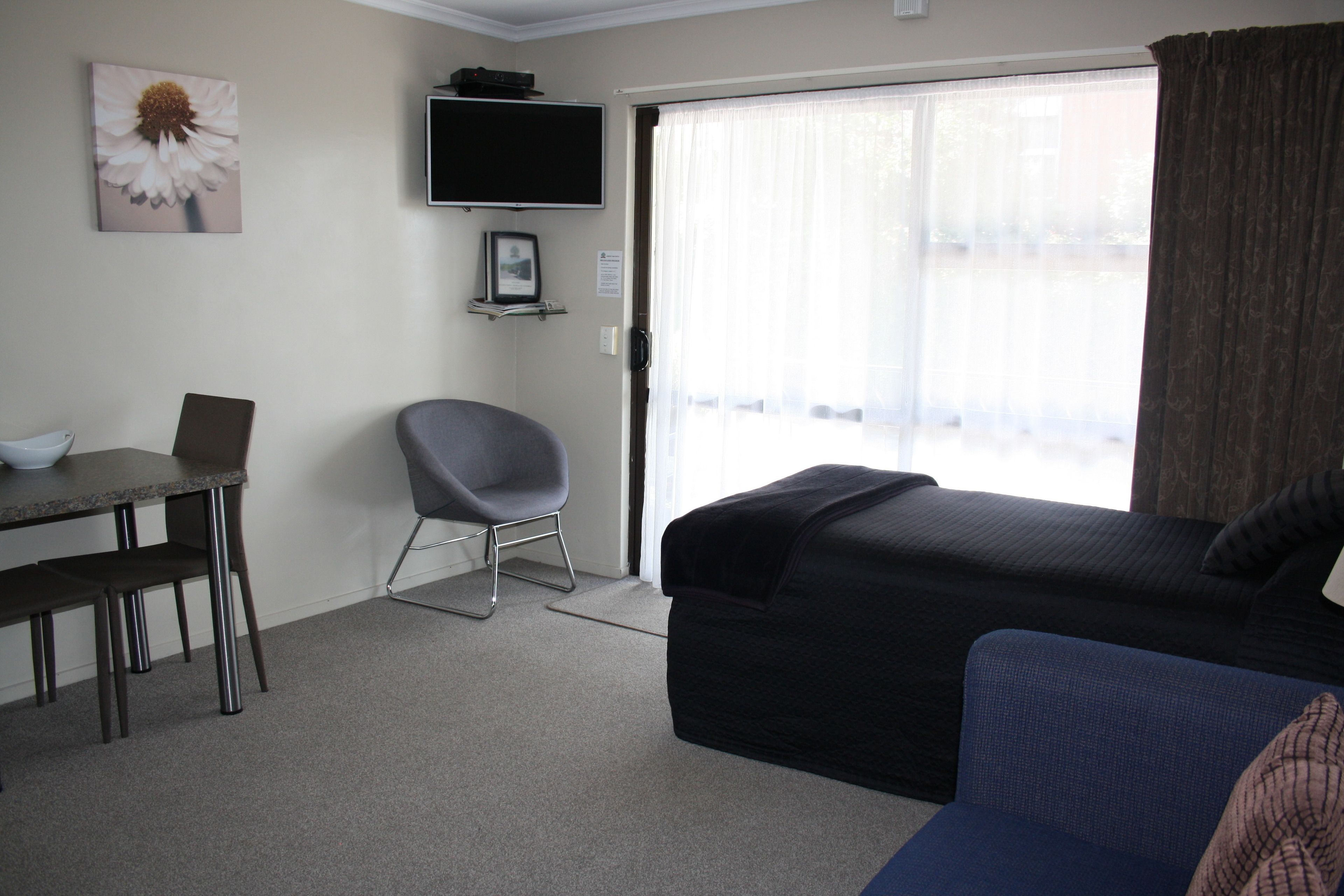 Habitación de hotel con cama, escritorio con computadora portátil, silla, televisor montado en la pared y ventana con cortinas.