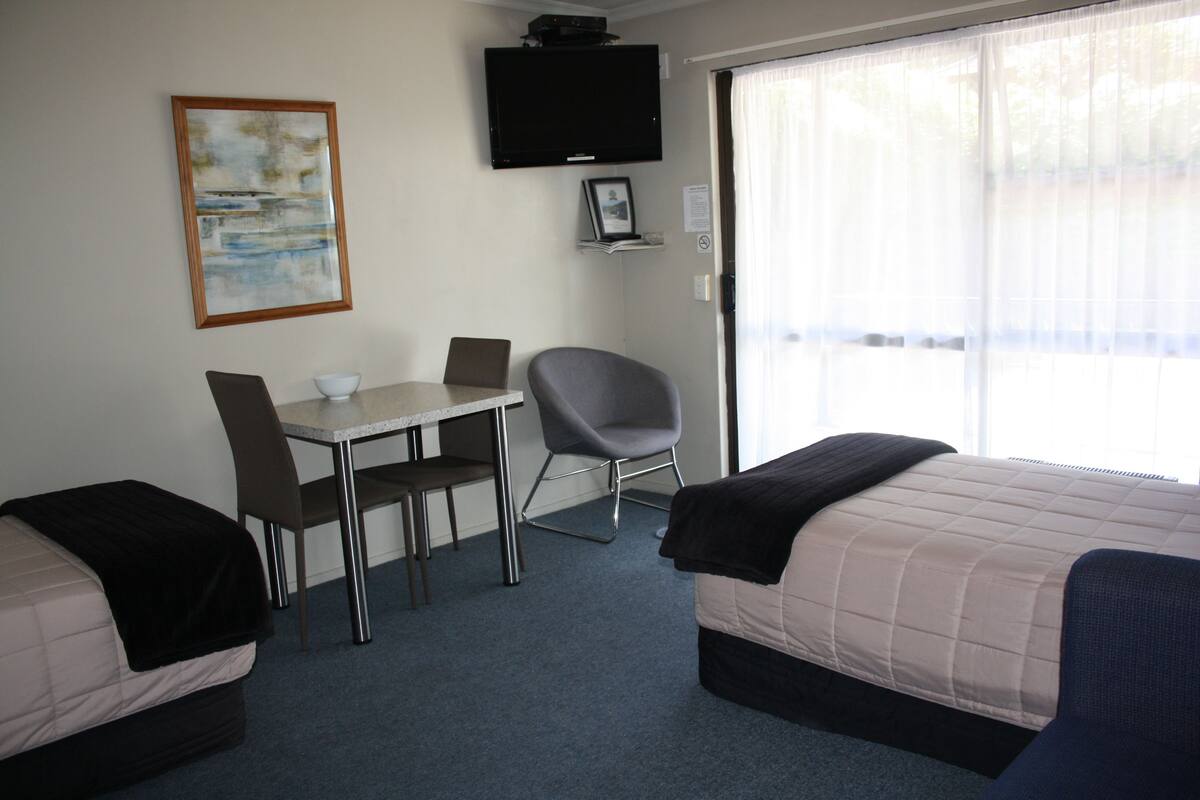A hotel room with two beds, a desk, a chair, a television, and a window with curtains.