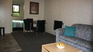 A living room with a sofa, a dining table with chairs, a TV, and a small table with a bowl.