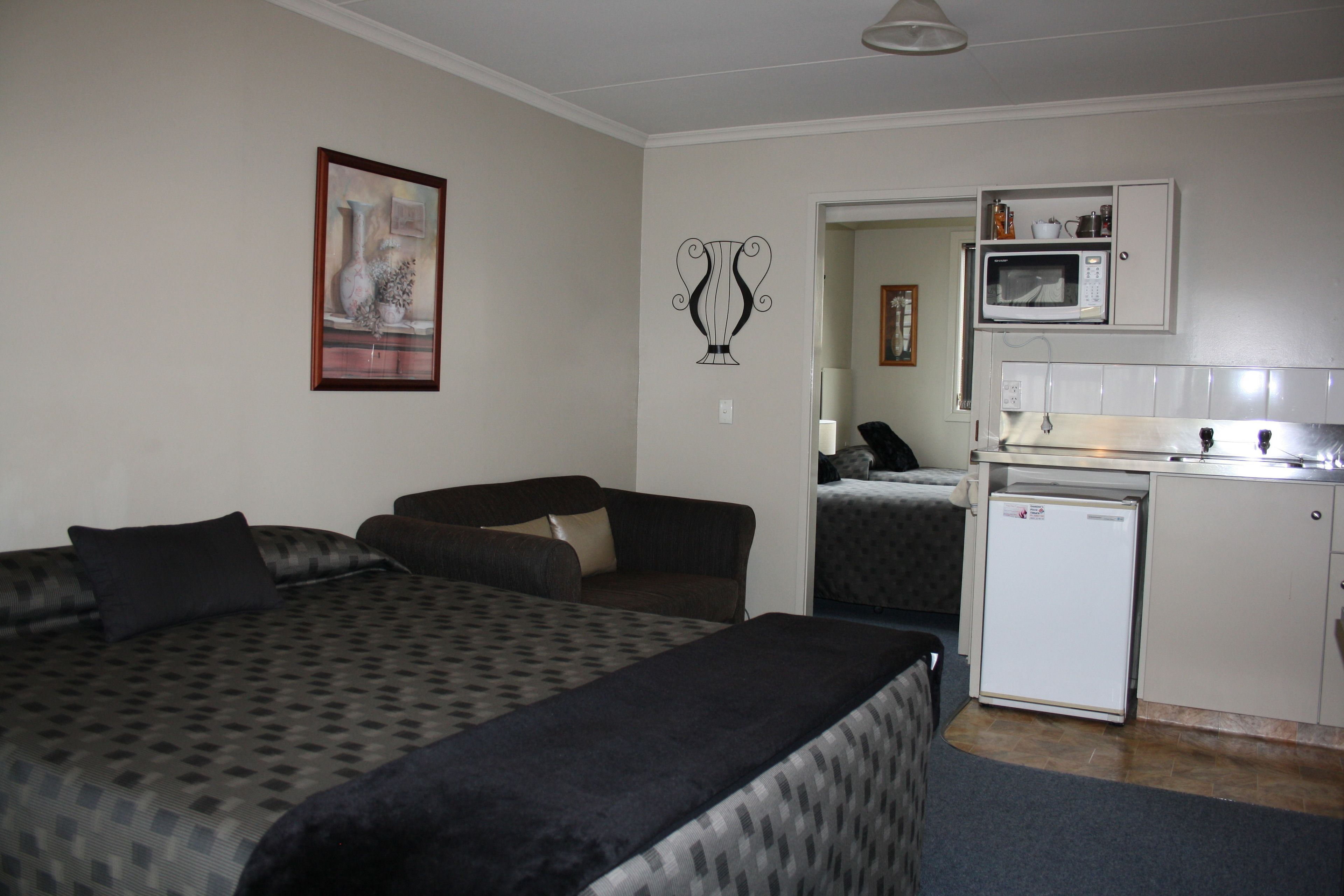 A compact room with a bed, a small kitchenette, and a door leading to another room.