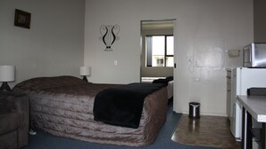 A hotel room with a bed, bedside tables, a small kitchenette, and a bathroom visible through an open door.