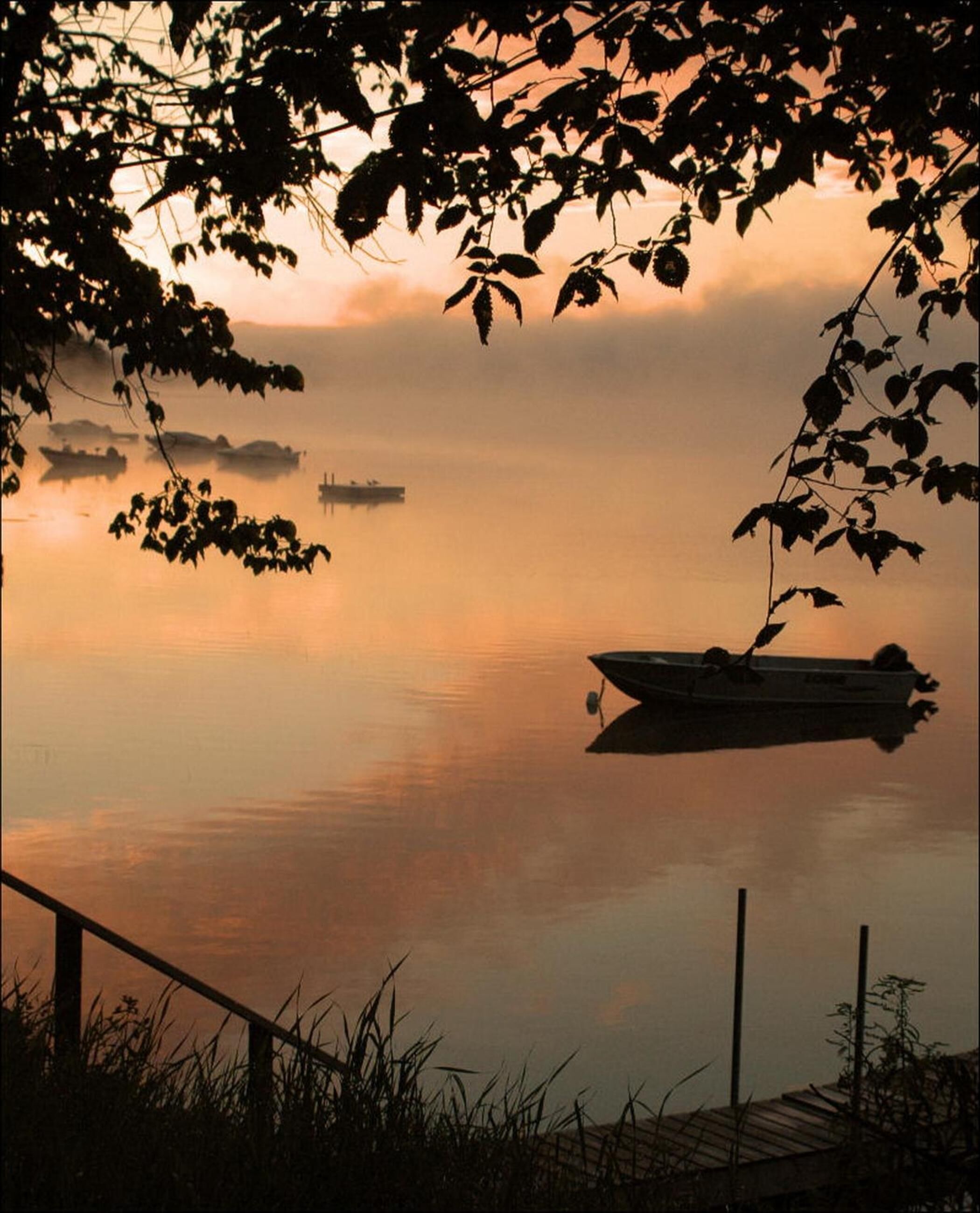 A calm lake with a boat docked on the right, surrounded by trees and a wooden dock.