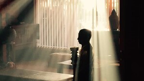 A room with a person standing near a window, sunlight streaming through blinds, and a visible chair and table. - Tantarra Guest House (Warners Bay)