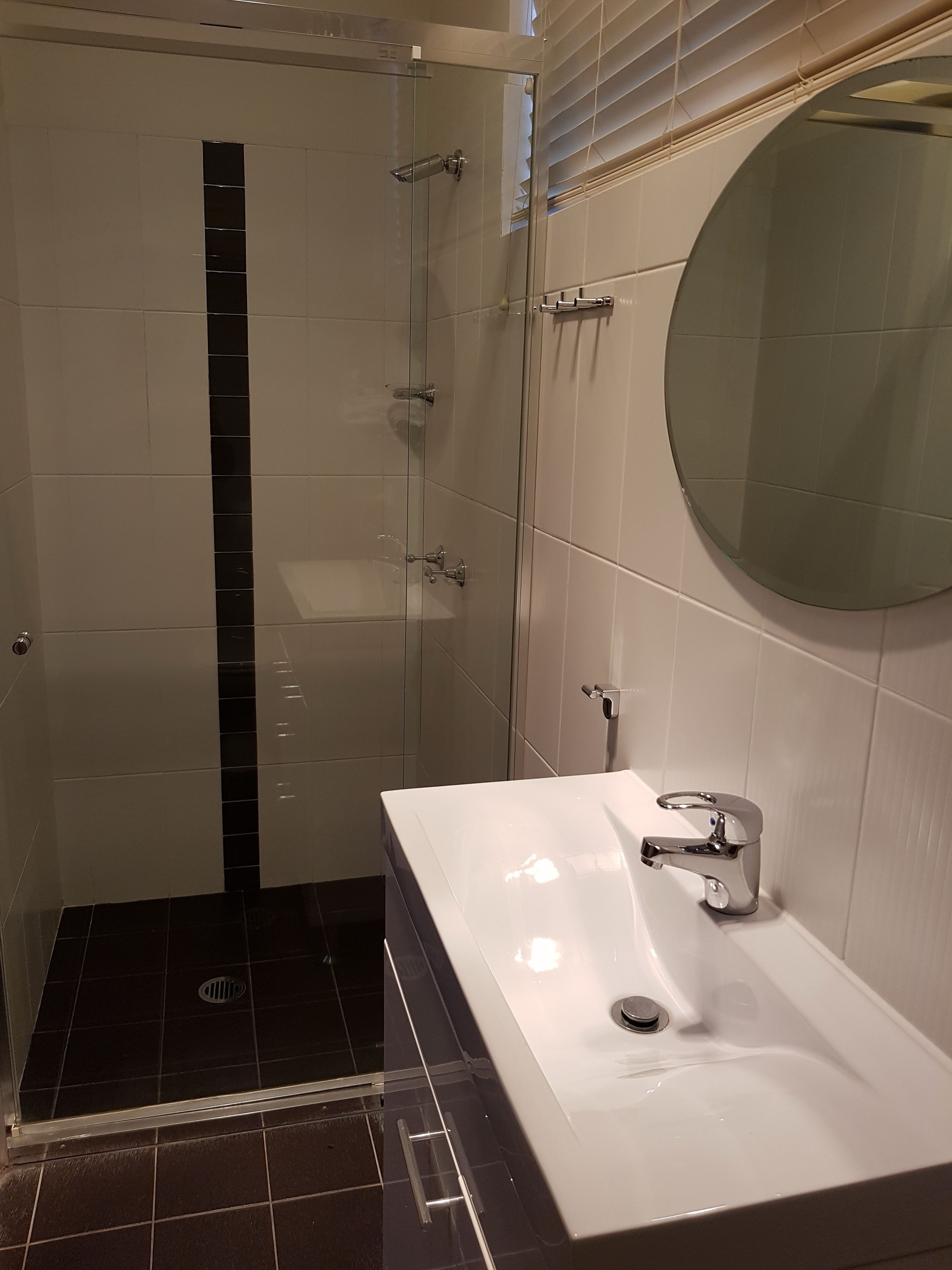 Une salle de bain moderne avec une douche à parois de verre, un lavabo blanc et un miroir rond.