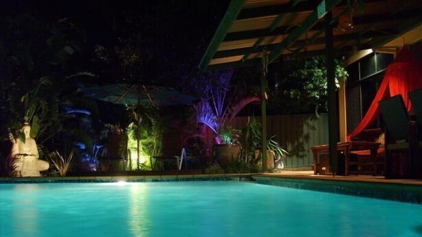 A nighttime pool area with a statue, potted plants, and a covered seating area. - Tantarra Guest House (Warners Bay)