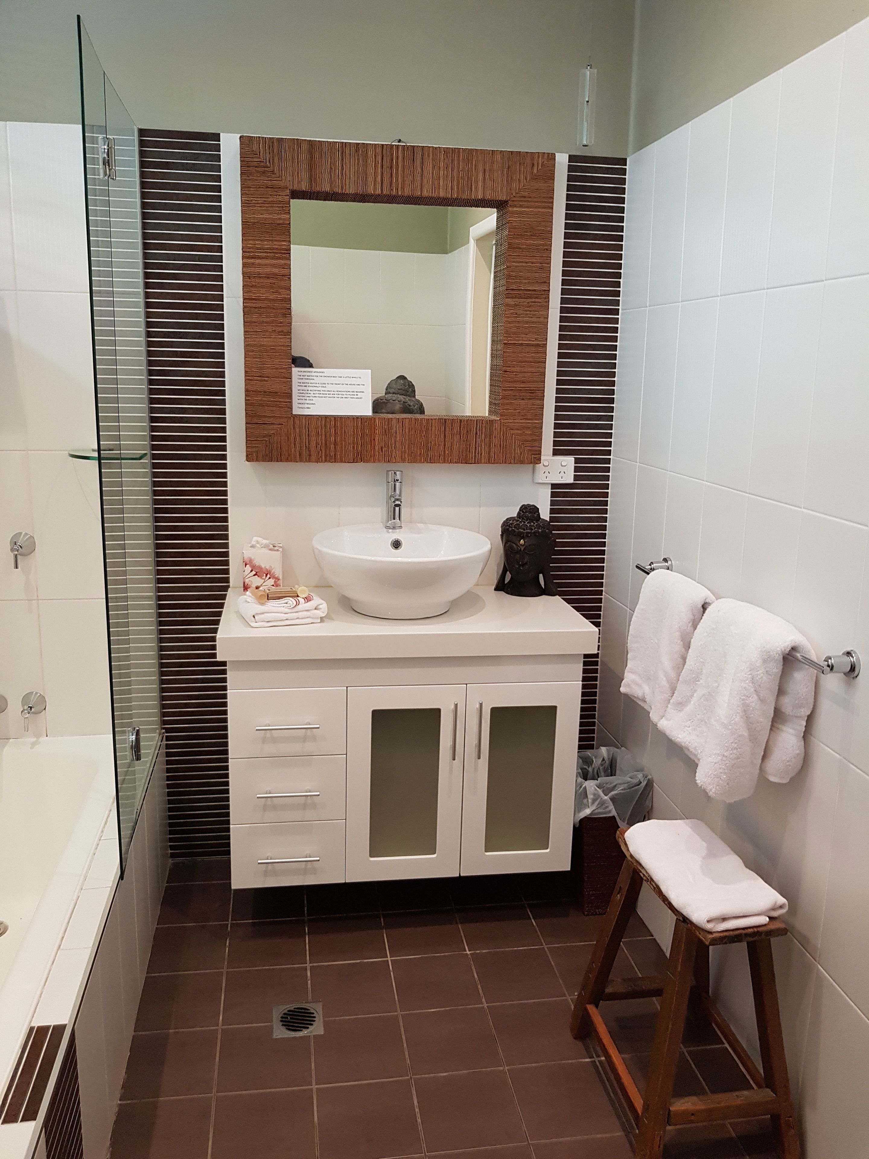 Un baño moderno con cabina de ducha de vidrio, lavamanos blanco sobre tocador de madera y toallero.