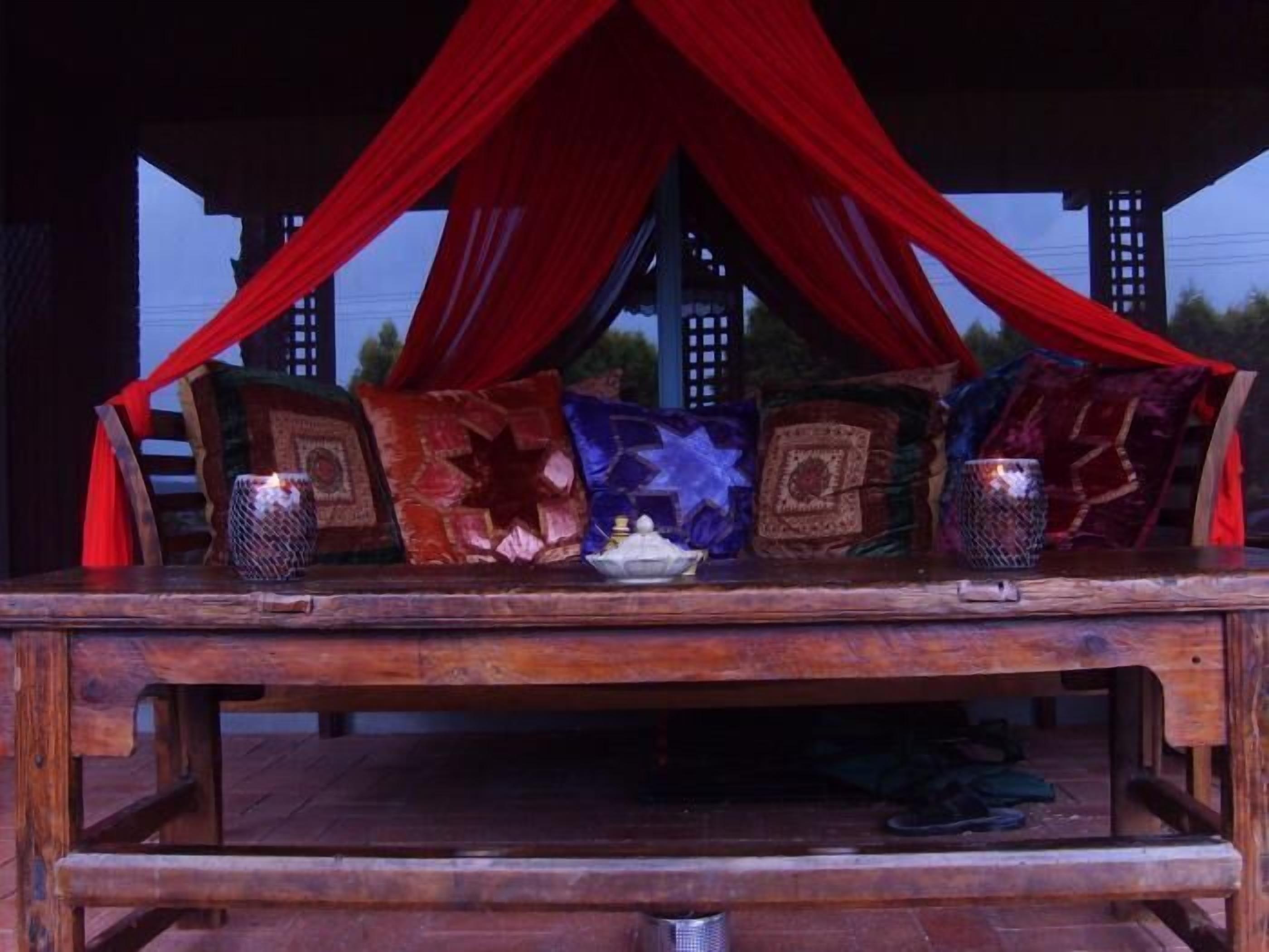 A wooden table with red drapes, decorated with patterned cushions and candle holders.