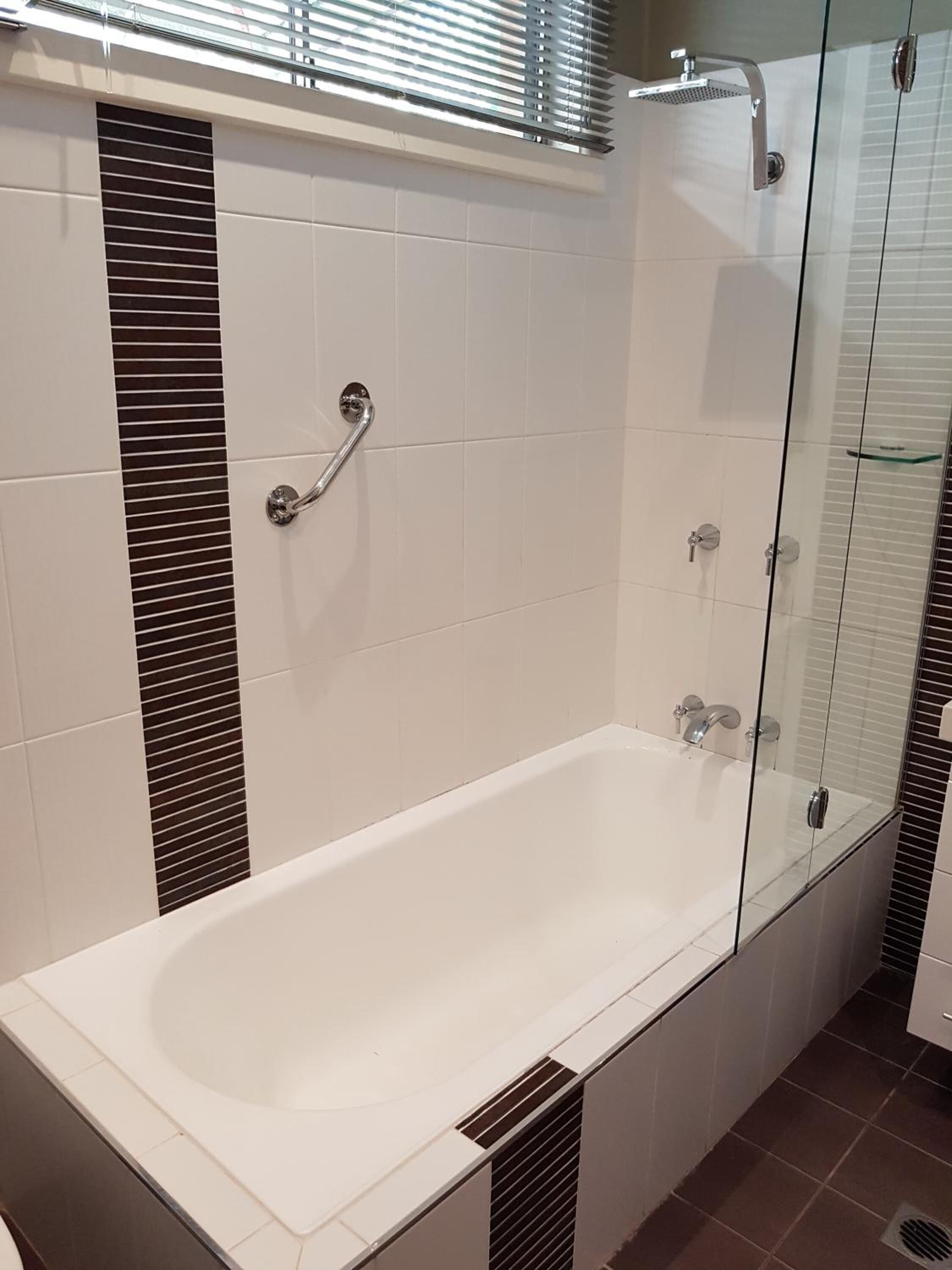 Une salle de bain moderne avec une douche à parois de verre, une baignoire blanche et une barre d’appui.
