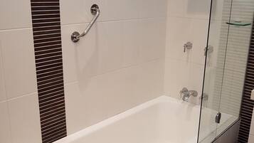 A modern bathroom with a glass-enclosed shower, a white bathtub, and a handrail.