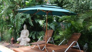 A wooden deck with two wicker lounge chairs and a green umbrella. - Tantarra Guest House (Warners Bay)