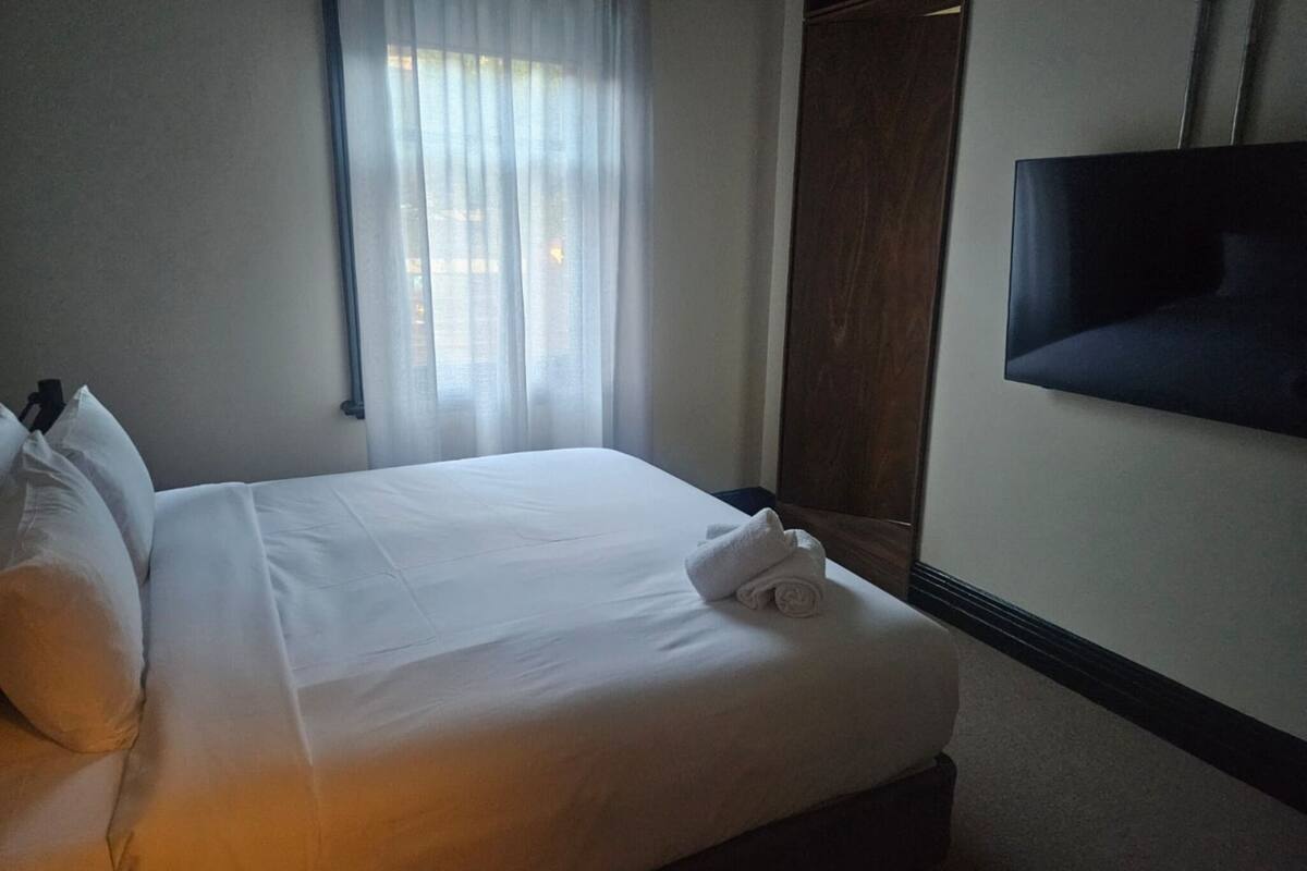 A neatly made bed with white linens, a folded towel, and a flat-screen TV mounted on the wall.