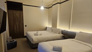 Quarto de hotel com duas camas, uma porta de madeira, uma mesa redonda pequena com garrafas de água e um lustre.