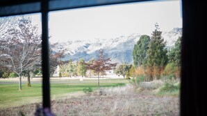 A view through a window of a grassy field with trees and mountains in the background. - Carrick Lodge Motel (Cromwell)