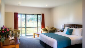 A hotel room with a bed, a desk, a chair, and a view of the outdoors. - Carrick Lodge Motel (Cromwell)