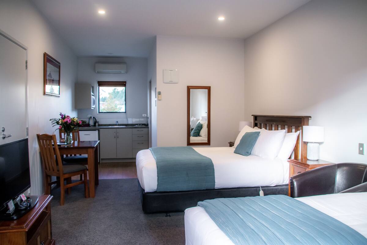 A hotel room with two beds, a desk, a TV, and a kitchenette.