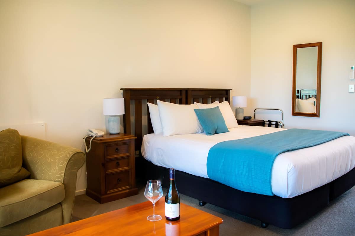 A hotel room with a bed, bedside table, lamp, and a chair.
