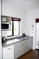 Una cocina moderna con armarios blancos, un microondas empotrado, un lavamanos de acero inoxidable y una ventana con persianas.