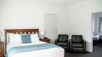 Una habitación de hotel con una cama, dos sillas, una mesita de noche y una puerta.