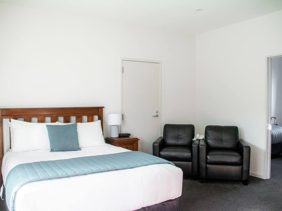 Una habitación de hotel con una cama, dos sillas, una mesita de noche y una puerta.