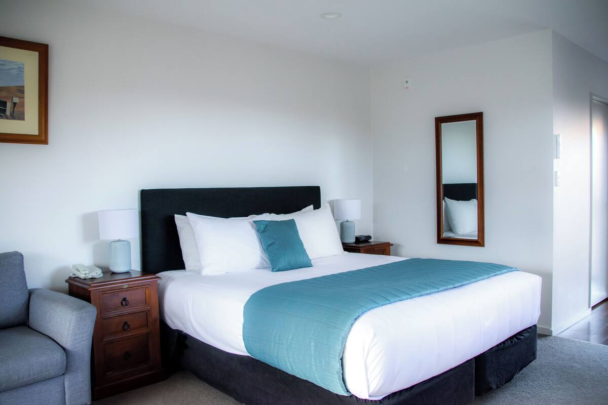 A neatly arranged bedroom with a bed, bedside tables, a chair, and a mirror.