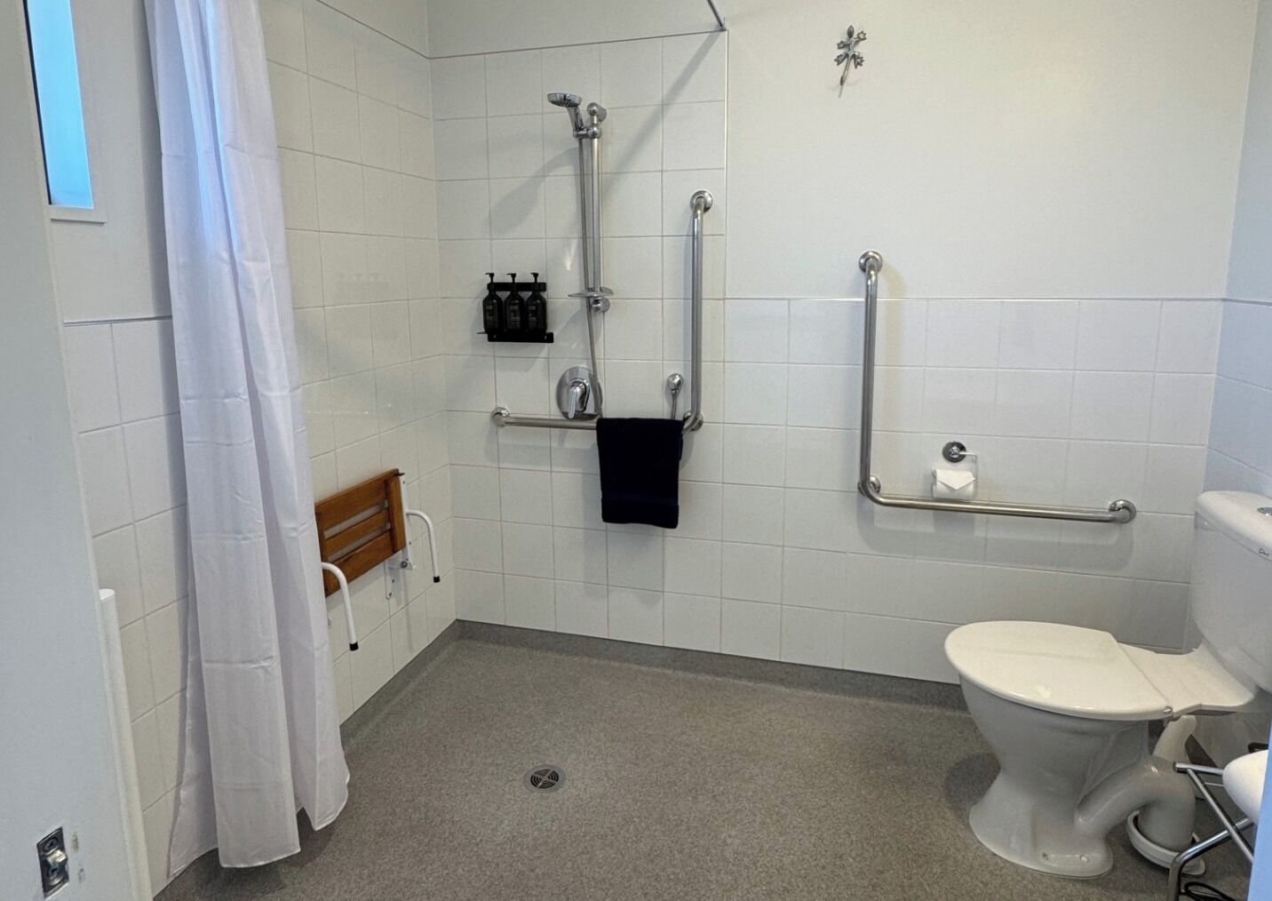 A wheelchair-accessible bathroom with grab bars, a shower, a toilet, and a bench.