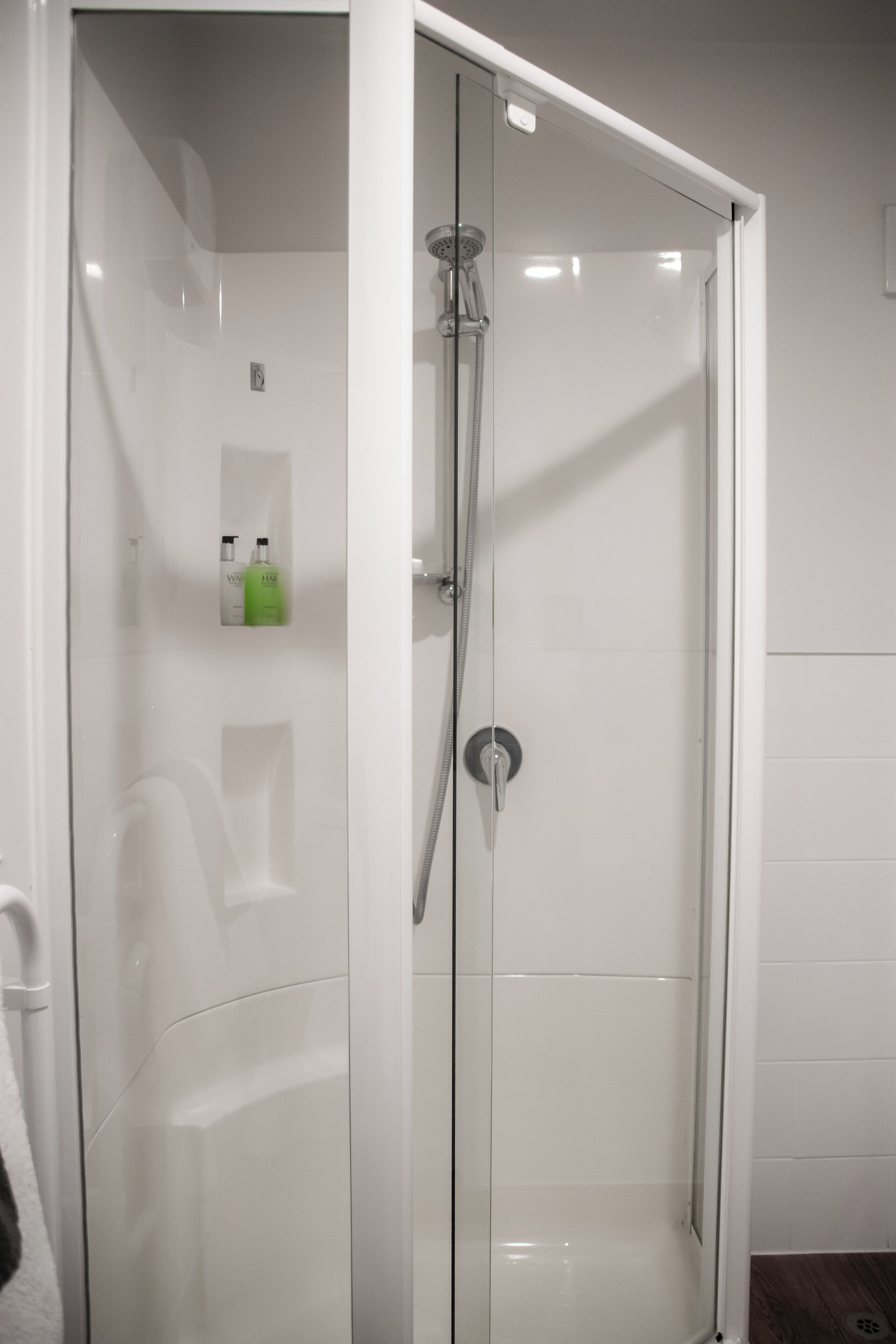 A glass-enclosed shower stall with a handheld showerhead and a wall-mounted faucet.