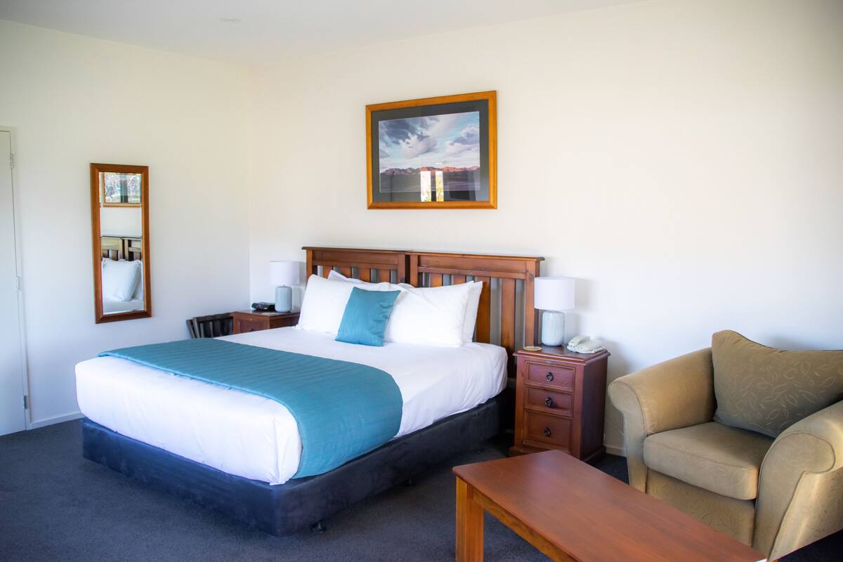 A hotel room with a large bed, bedside tables, a chair, and a wooden headboard.