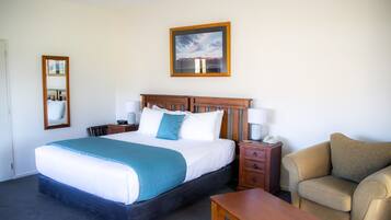 A hotel room with a large bed, bedside tables, a chair, and a wooden headboard.
