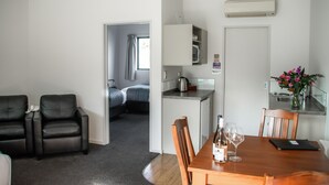 A modern hotel room with a dining area, a kitchenette, a bed, and a bathroom. - Carrick Lodge Motel (Cromwell)