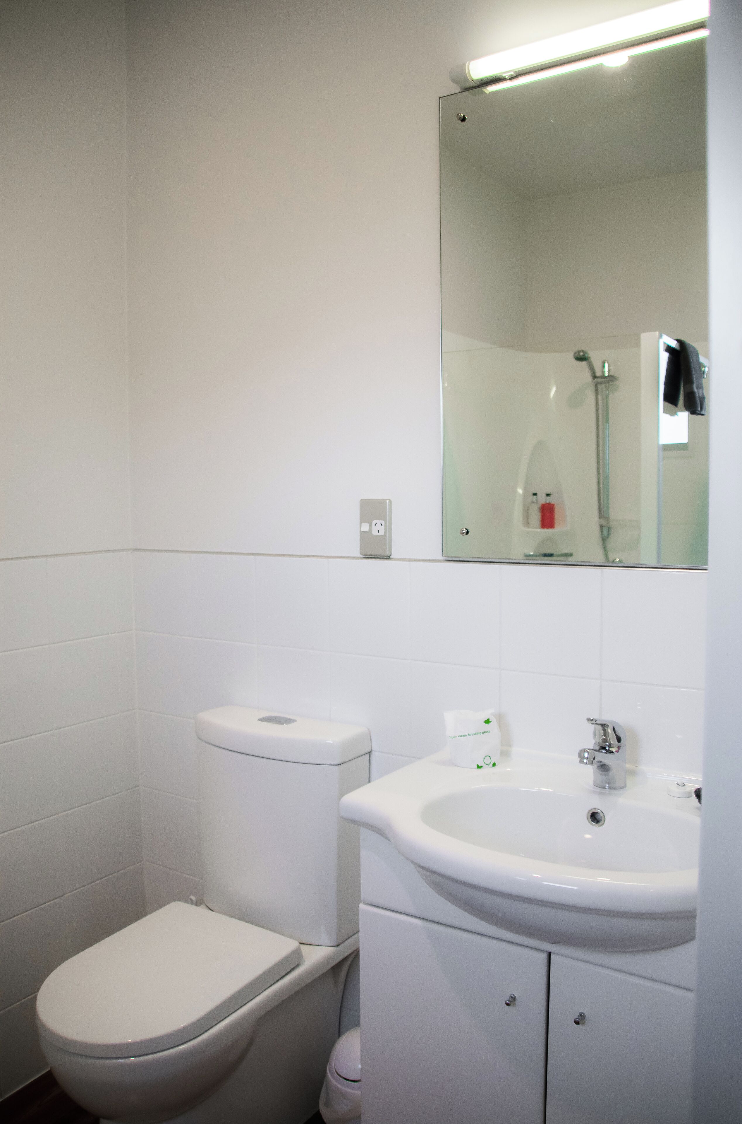 A bathroom with a toilet, sink, mirror, and a shower area.