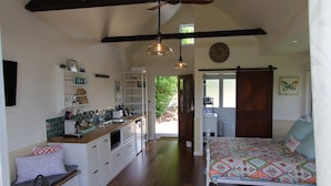 Habitación amplia con cama, escritorio y kitchenette. Se ve un ventanal con vistas a zonas verdes.