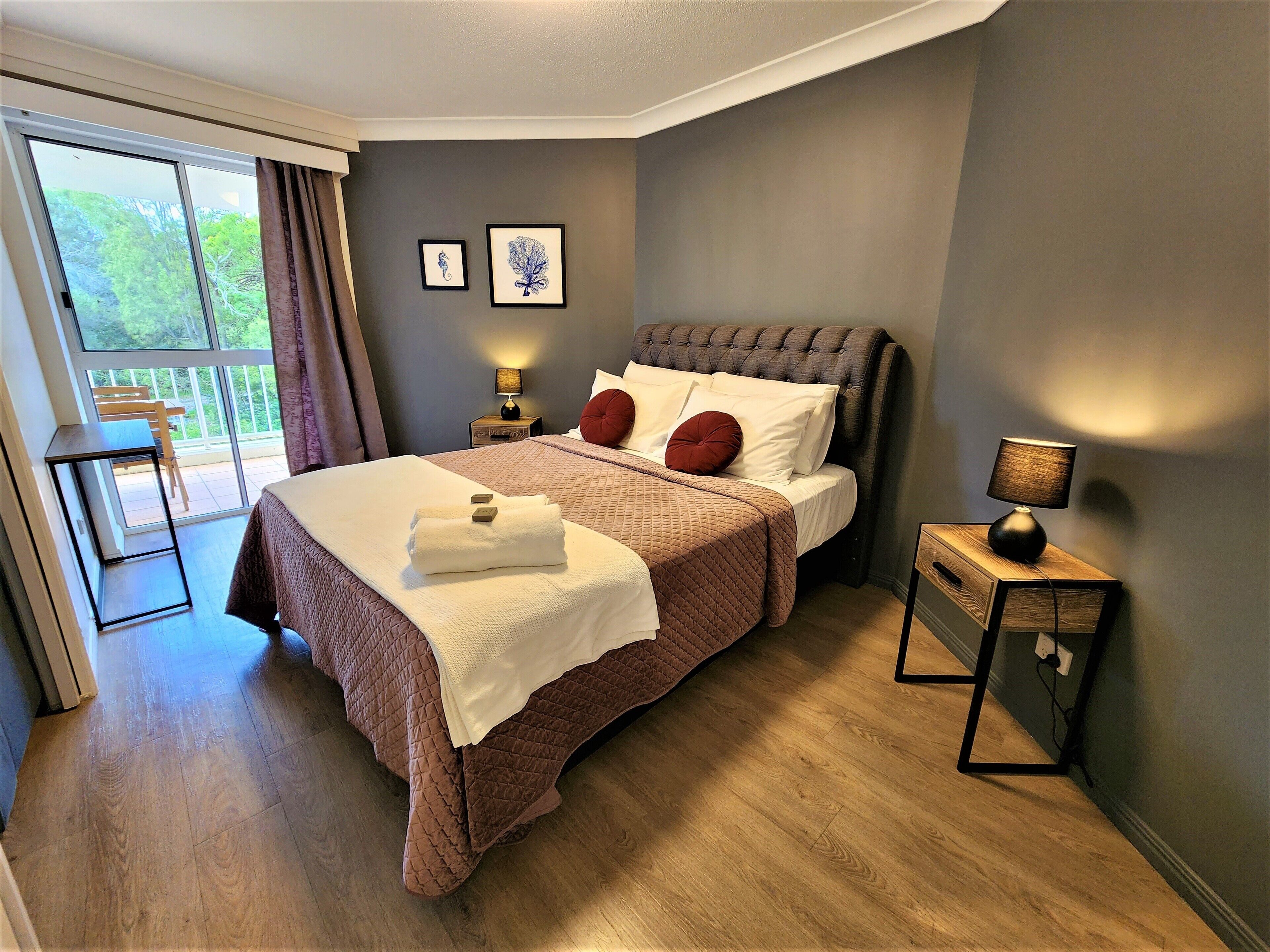 A neatly made bed with a brown quilt, a bedside lamp, and a framed picture on the wall.
