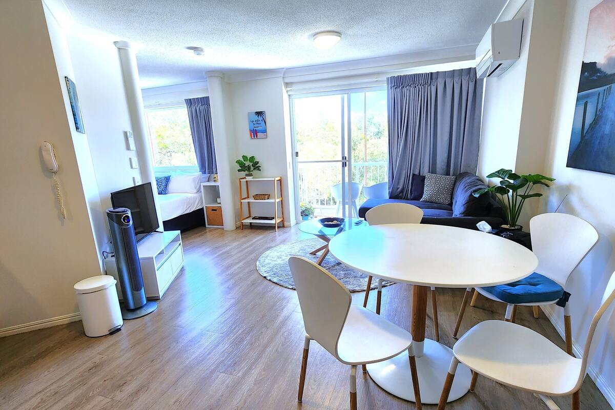 A modern living room with a round dining table, white chairs, a sofa, and a TV.