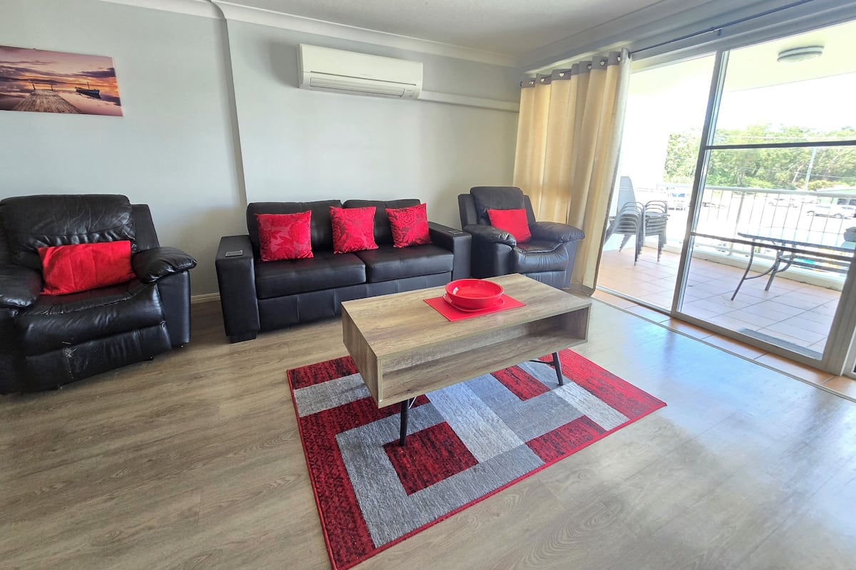 A modern living room with a black leather sofa, a wooden coffee table, and a red rug.
