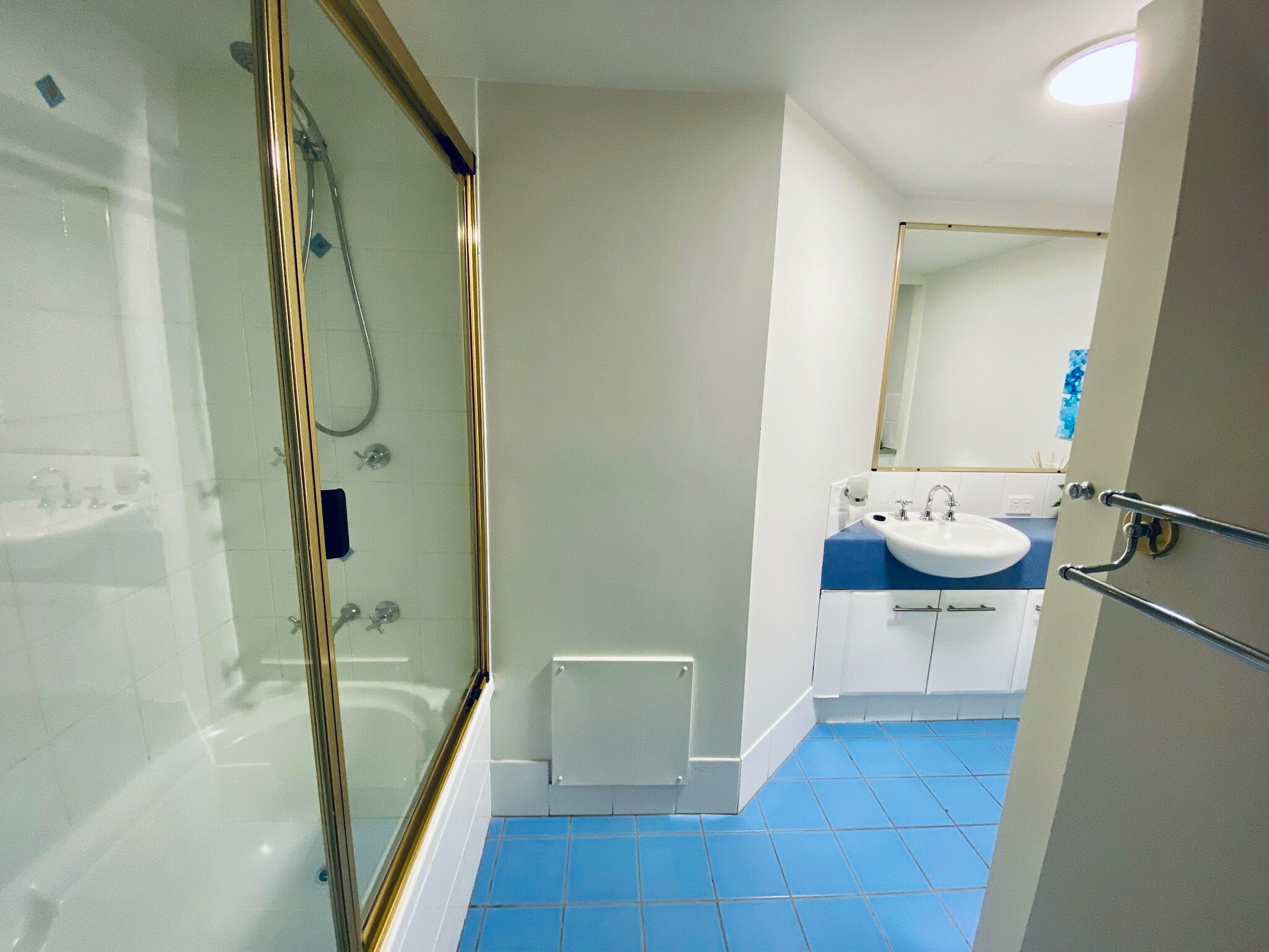 A bathroom with a glass-enclosed shower, a white sink, and a blue-tiled floor.