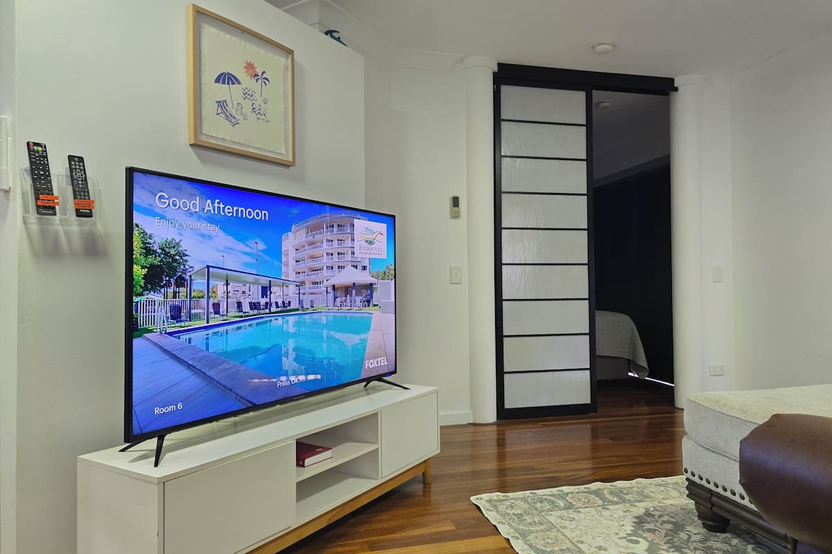 A television displaying a poolside view, a framed picture, and a white entertainment unit.