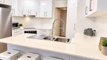 Una cocina moderna con armarios blancos, un lavamanos de acero inoxidable, un horno empotrado y un microondas.