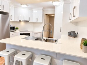 A modern kitchen with white cabinetry, a stainless steel sink, a built-in oven, and a microwave. - Fairways Golf & Beach Retreat (Woorim)