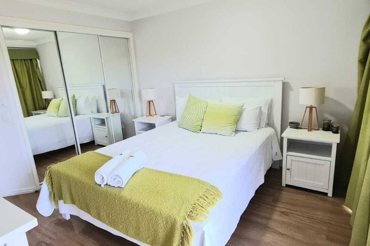 A hotel room with a bed, a nightstand, a mirror, a wardrobe, and a green curtain.
