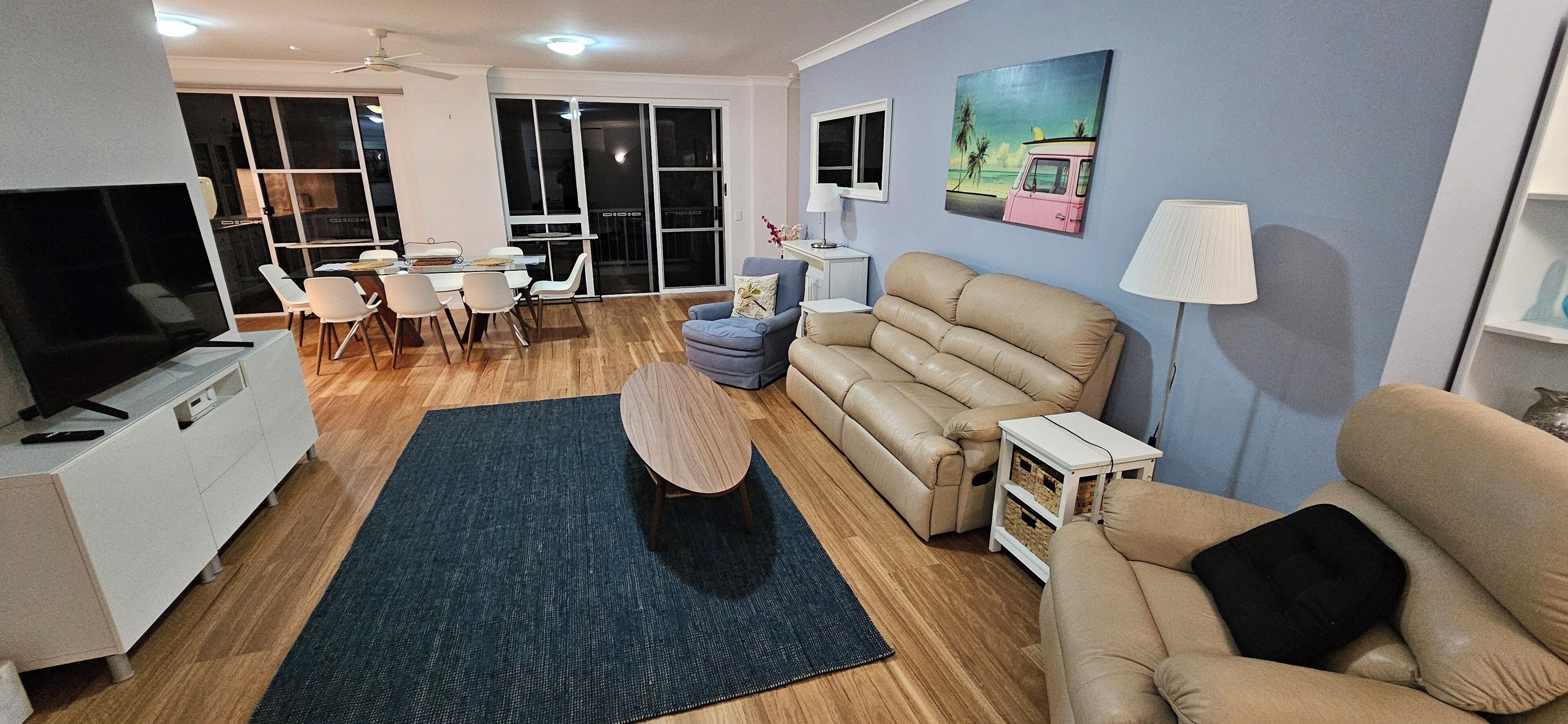 A living room with a sofa, a TV, a dining area with chairs, and a painting on the wall.