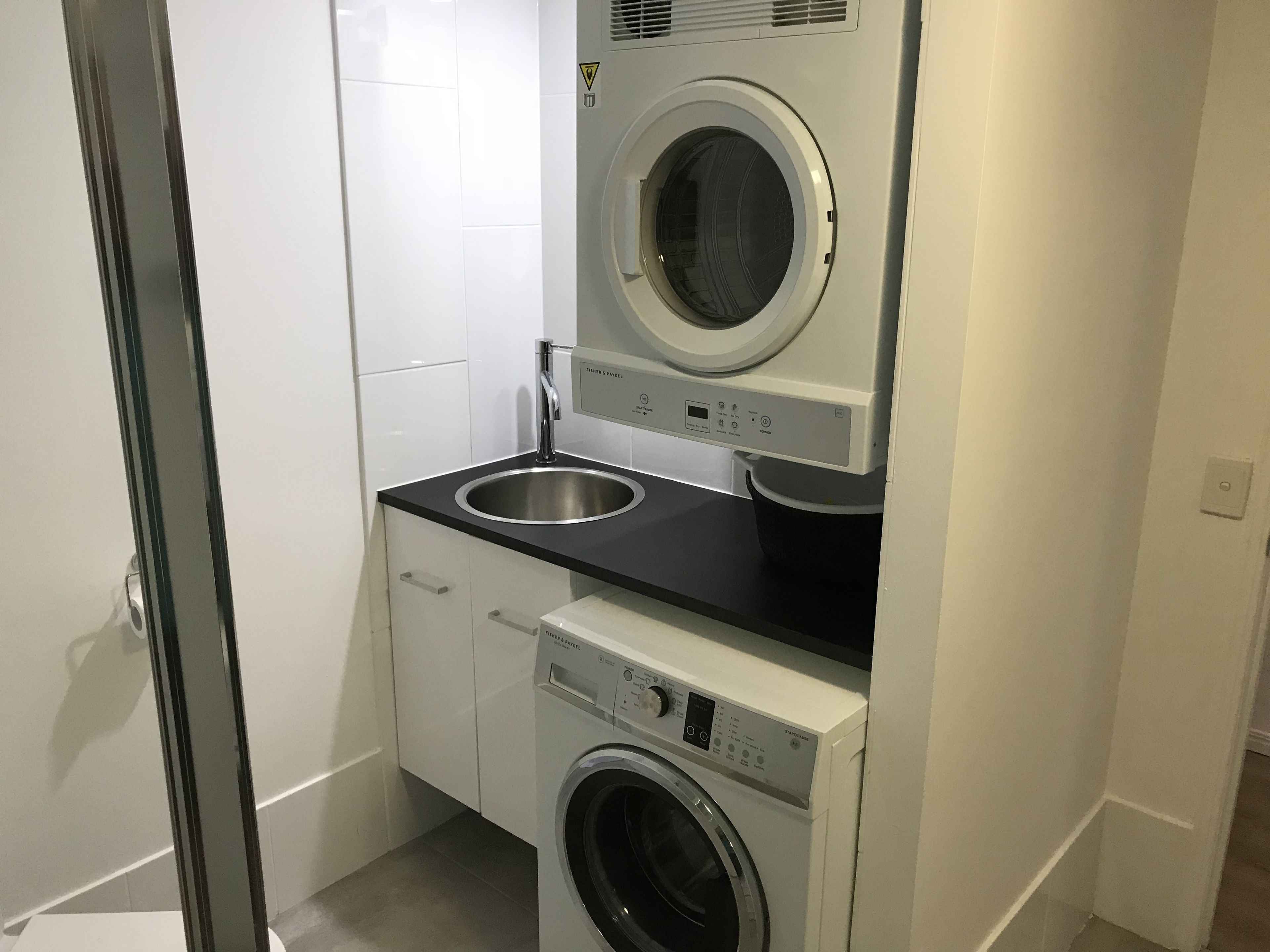 A compact laundry room with a front-loading washer and dryer, a sink, and a cabinet.