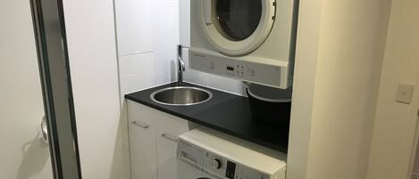 A compact laundry room with a front-loading washer and dryer, a sink, and a cabinet.